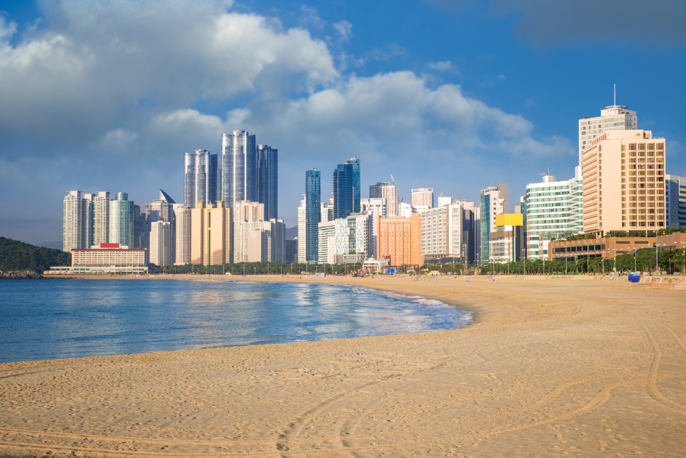 Sunny day over the sandy Haeundae Beach with skyscrapers in the background.