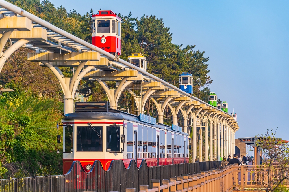 Red train next to a walking path and under colorful rail cars.