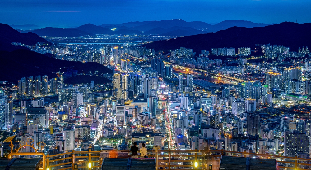 Looking down at Busan lit up at dusk with skyscrapers and mountains.