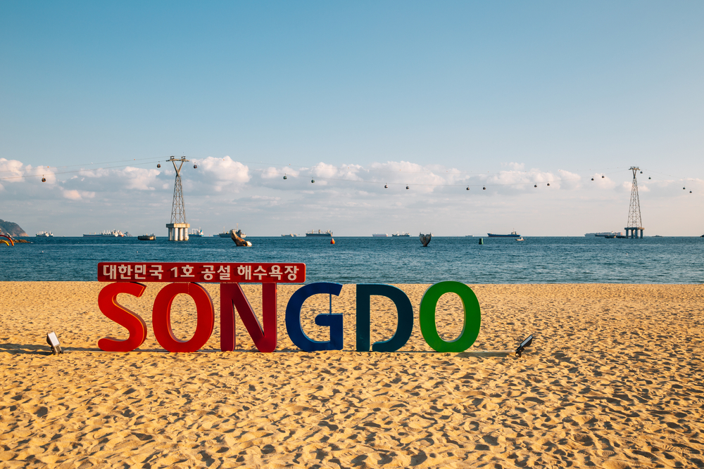 Colorful sign reading Songdo on a sandy beach at golden hour with a cable car in the background.