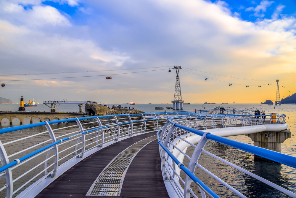 Sunset over the Songdo Skywalk twisting over the ocean with cable cars in the distance.