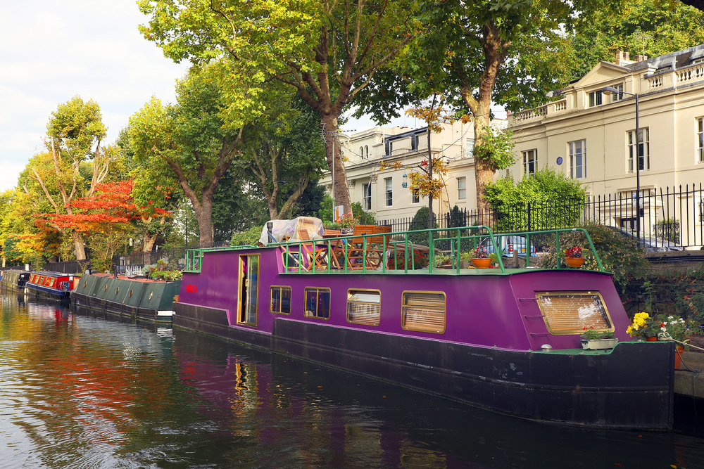 Little Venice water channels in London.  The picture shows a purple canal boat There are houses behind and a canal path. One of the romantic things to do in London 