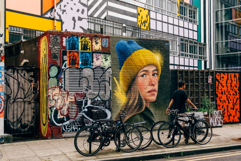  Bicycles parked on Redchurch Street in Shoreditch. There is street art on the wall and a man walking past. 