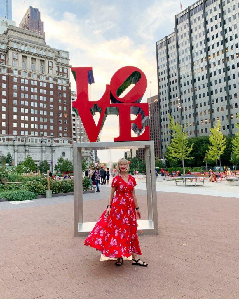 Caucasian woman in red dress in front of LOVE statue one of the best things to do in Philadelphia.