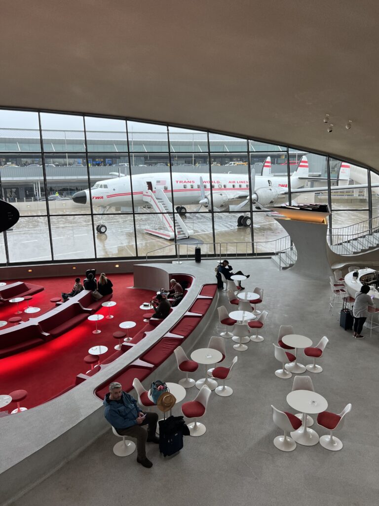 View of the sunken lunge from above. It's red with white tables and you can see the airplane cocktail bar in the background.  
