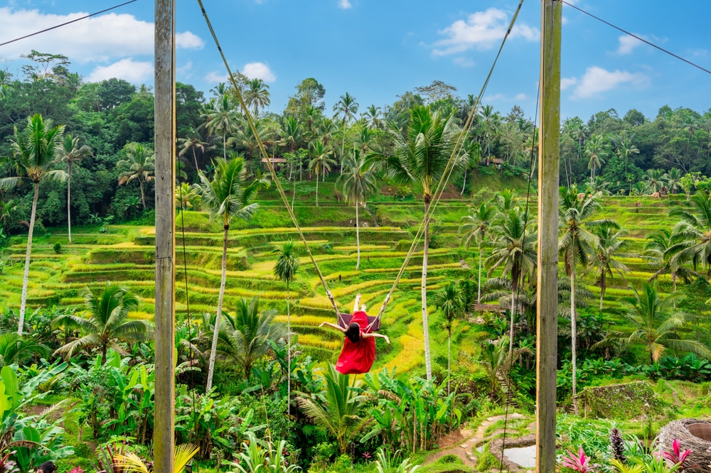 Young female tourist in red dress enjoying the Bali swing at tegalalang rice terrace in Bali, Indonesia. One of the 50th birthday trip ideas