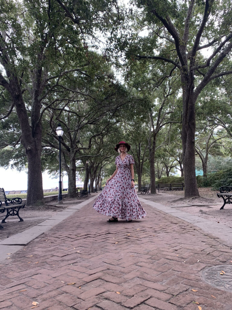 woman in long dress standing on a path covered with trees