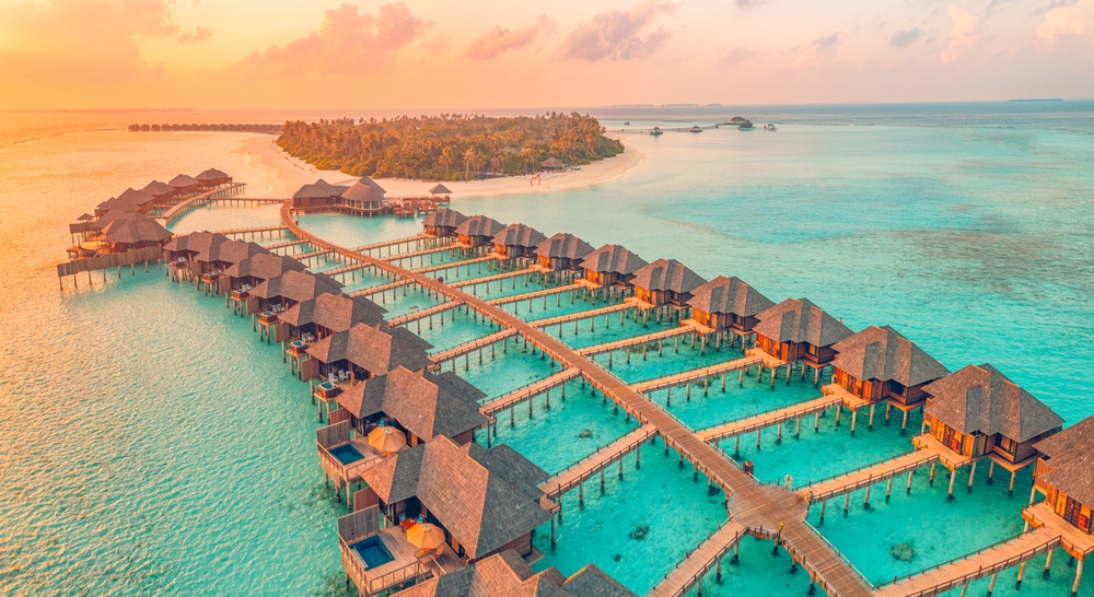 Aerial sunset panoramic landscape luxury tropical resort water villas. Beautiful island beach orange sunrise sea sky. Amazing bird eyes panorama Maldives paradise tropical bay. Exotic summer vacation. A wonderful 30th birthday trip ideas