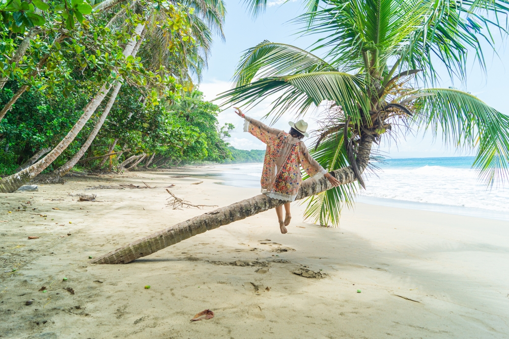 Woman sat on a palm tree on the beach in a tropical paradise. Costa Rica, Caribbean coast. 30th birthday trip ideas