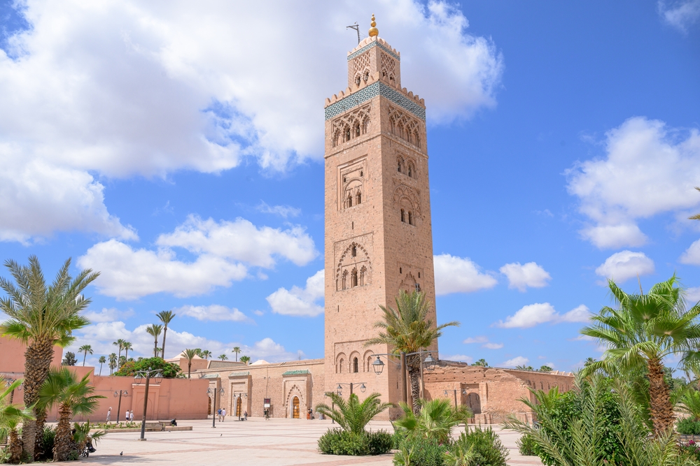 Day time landscape of Koutoubia mosque , Marrakech. The sky is blue and there are palm trees around the mosque tower. 