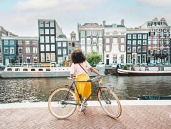 girl with cycle in front of canal with buildings and boats in the backdrop