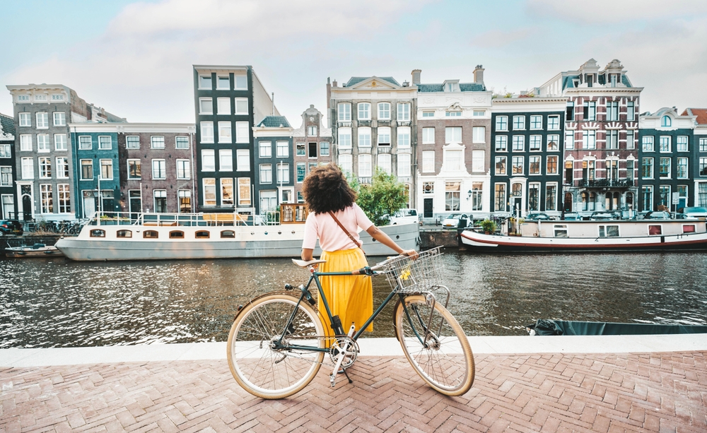 girl with cycle in front of canal with buildings and boats in the backdrop