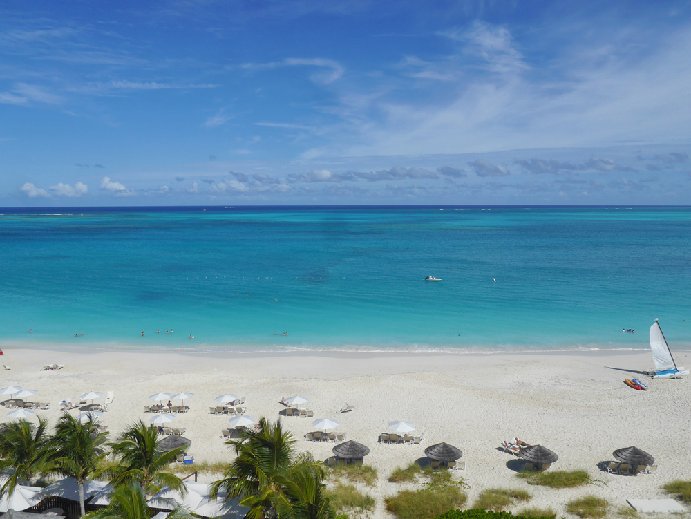 Beach taken from above with umbrellas and bright blue water. 