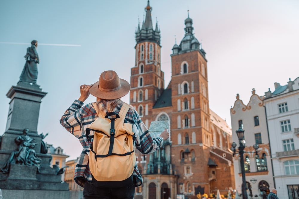 Back view of traveller woman walking on old Market Square in Krakow holding tourist map. The article is about traveling to Europe. 