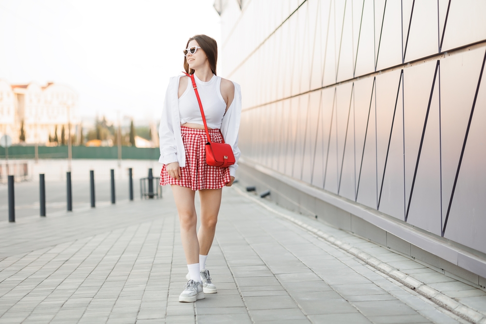 woman white shirt and red gingham skirt walks down city sidewalk.