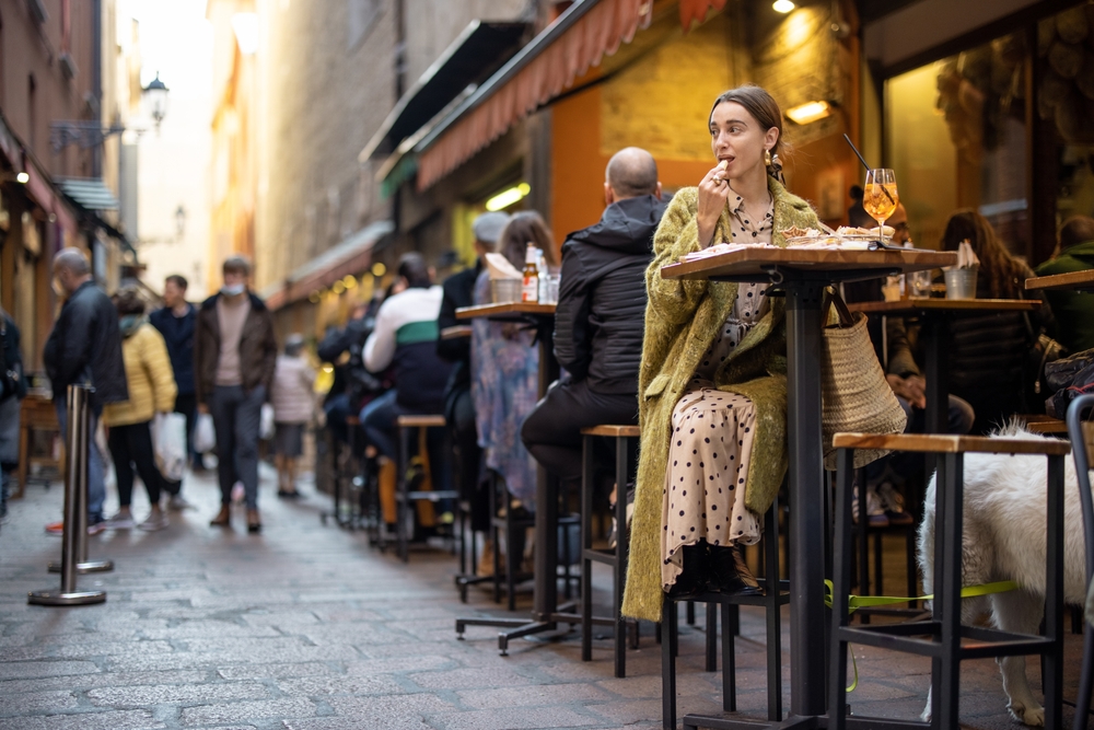 Woman sitting on crowded street at bar or restaurant outdoors. 