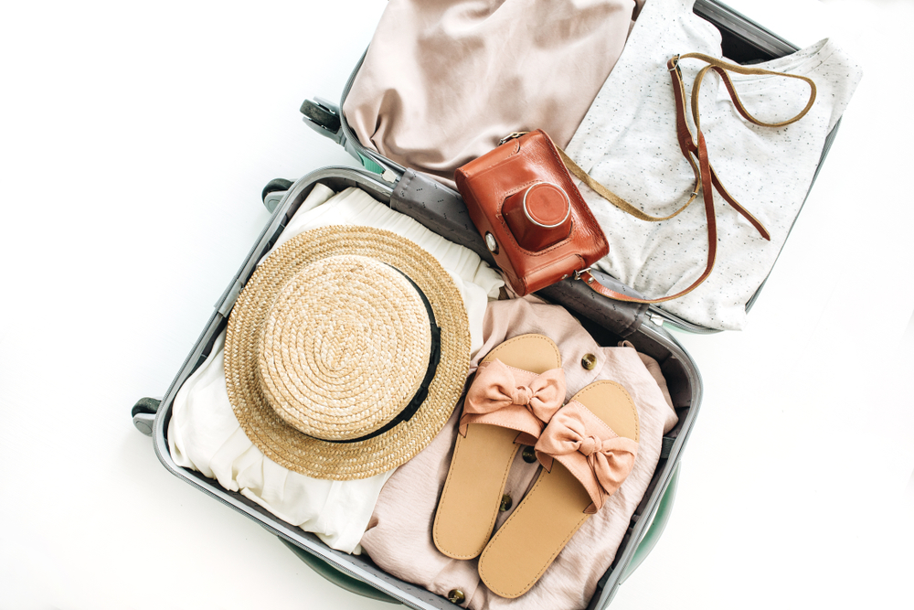 Overhead picture of a packed suitcase with clothing, a sun hat, shoes, and a camera.