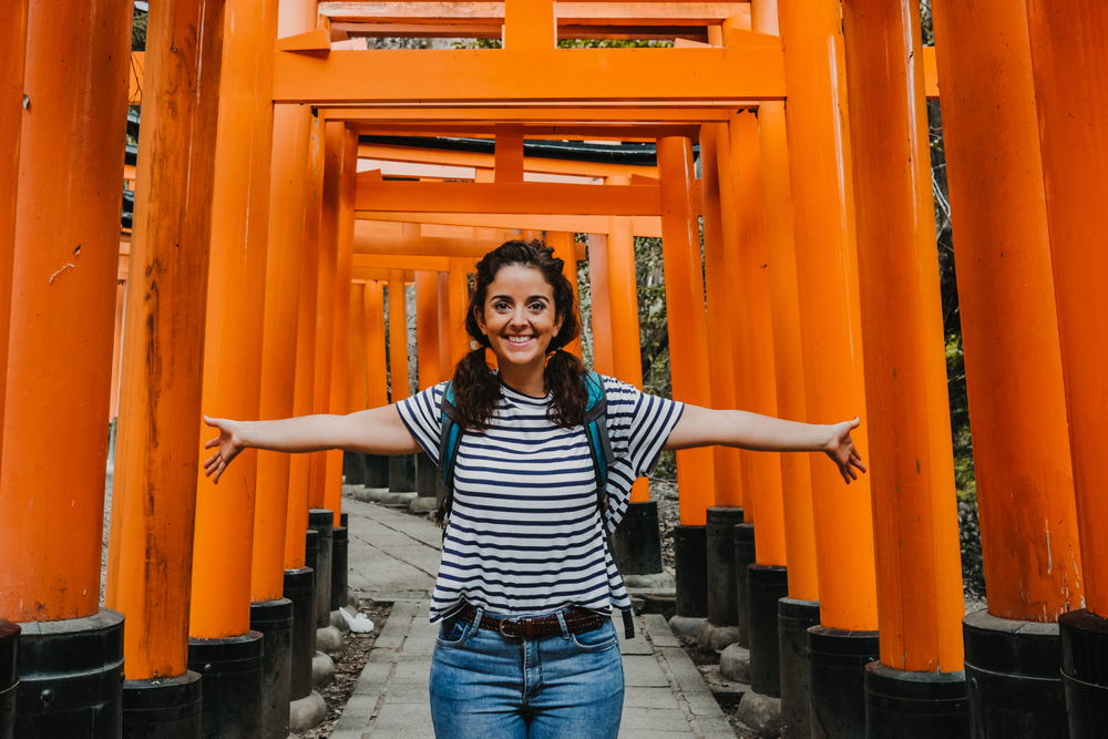 Smiling woman under torii gates wearing a striped, short-sleeved shirt.