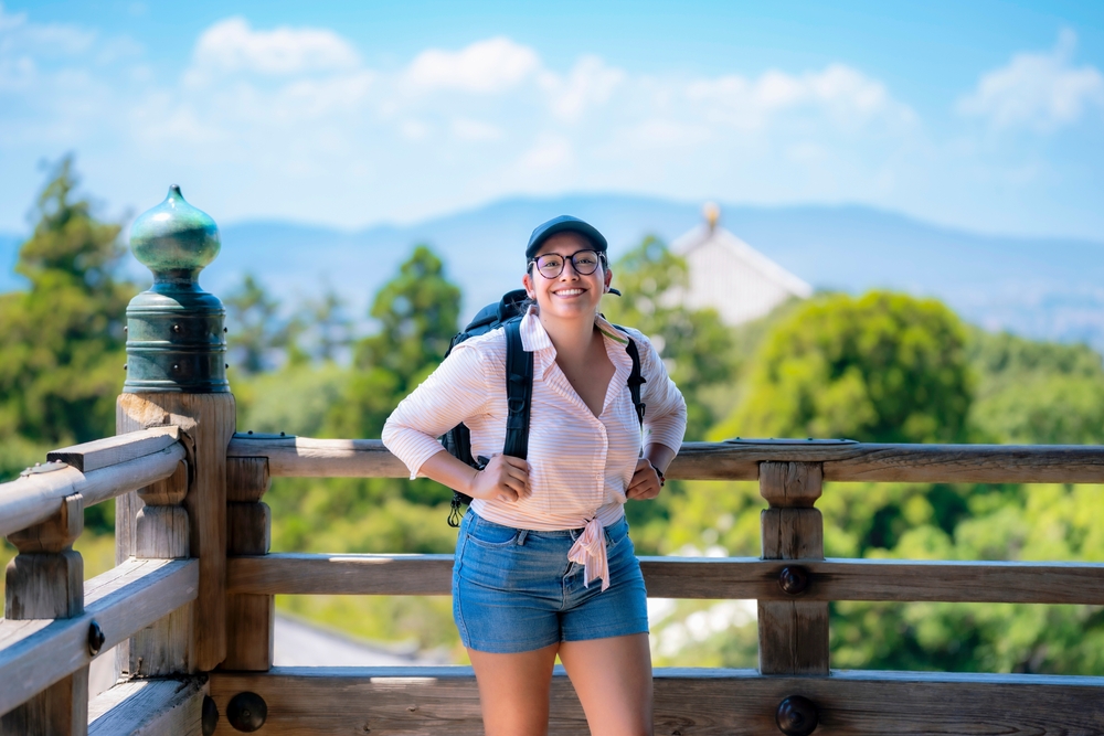 Young woman wearing a lightweight blouse, shorts, backpack, and hat,  great idea for What to Wear in Japan in Summer.