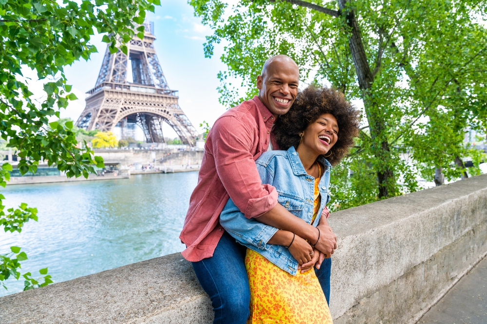 Hugging couple sitting along the Seine River with the Eiffel Tower in the background.