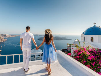 A couple holding hands overlooking the ocean in Santorini, Greece, one of the best honeymoon destinations in the world.