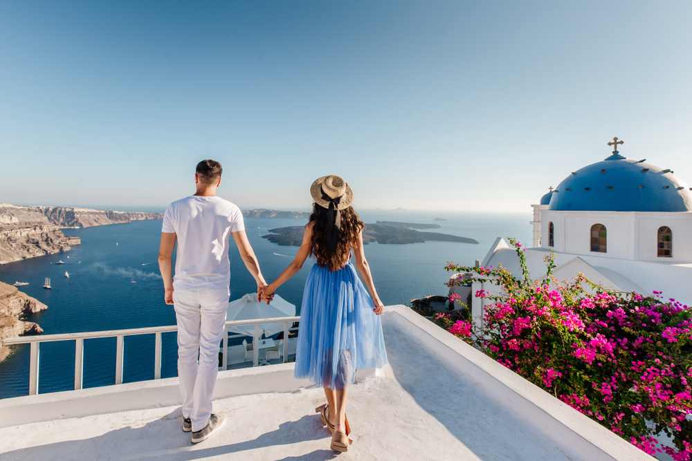 A couple holding hands overlooking the ocean in Santorini, Greece, one of the best honeymoon destinations in the world.