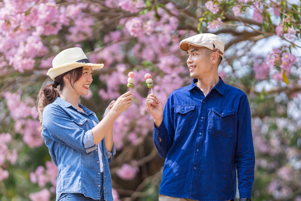 Couple holding a colorful treat under pink cherry blossoms in Japan.