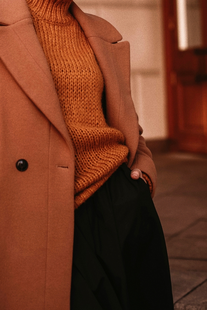 A close up of a brown jumper, brown coat and black trousers. The article is about outfits in winter in London. 