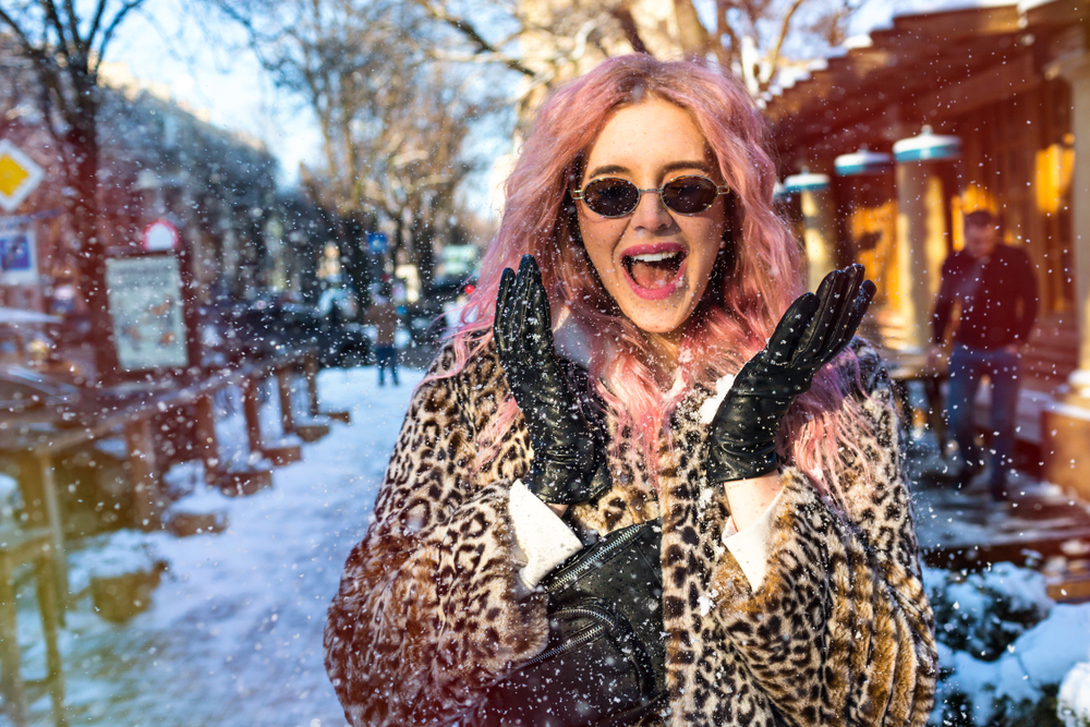 girl with smile in London when it is snowing. She has black gloves and coat.  The article is about winter in London. 