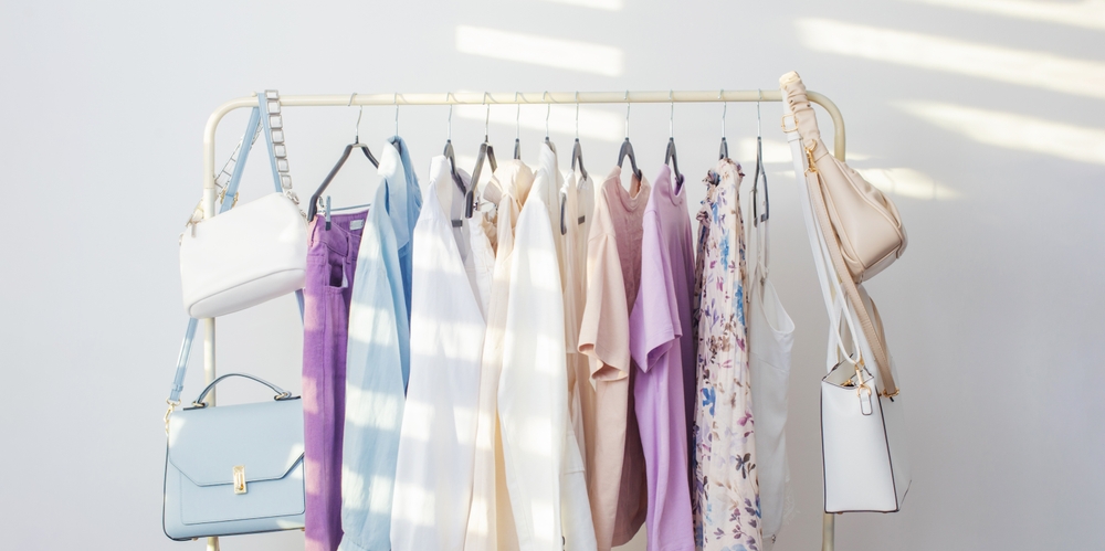 A rail of summer London outfits in pastel colors with handbags hanging from the rail. 