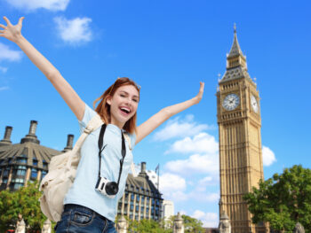 large tower in background with woman smiling carring carera around her neck in foreground