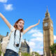 large tower in background with woman smiling carring carera around her neck in foreground