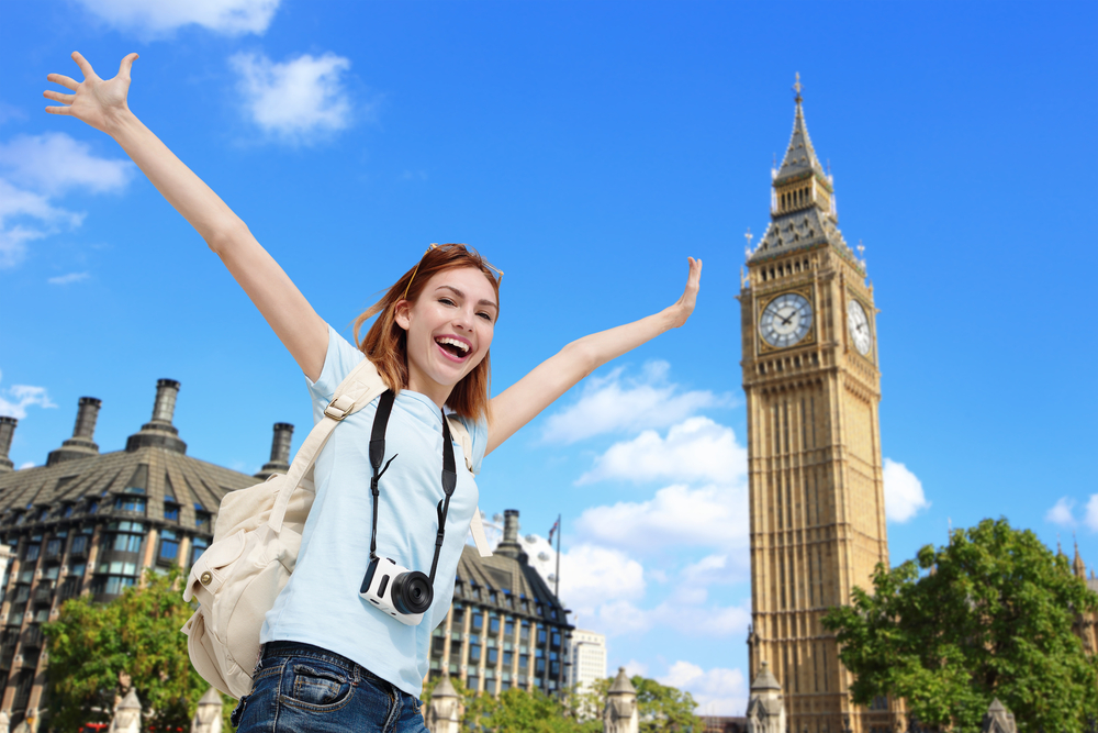 large tower in background with woman smiling carring carera around her neck in foreground