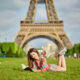 girl lying down on grass in front of eiffel tower reading a book in colorful dress paris outfit ideas