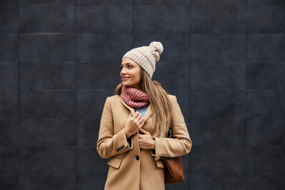 Smiling woman wearing a beanie, scarf, and wool trench coat, one of the best outfits in Japan for winter.