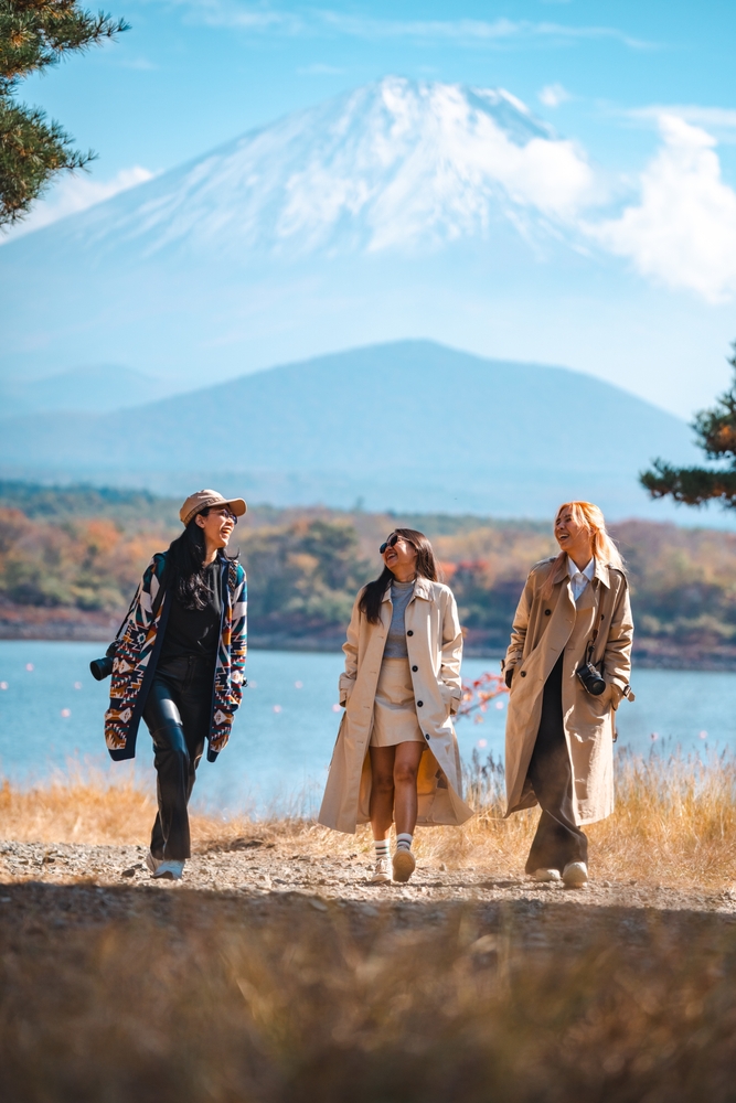 Three young women walking along a lake with Mount Fuji in the background showing off what to wear in Japan in the fall.