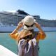 Photo of a woman from the back looking out at a cruise ship, holding her hat, and wearing a backpack. Caribbean Cruise Packing List