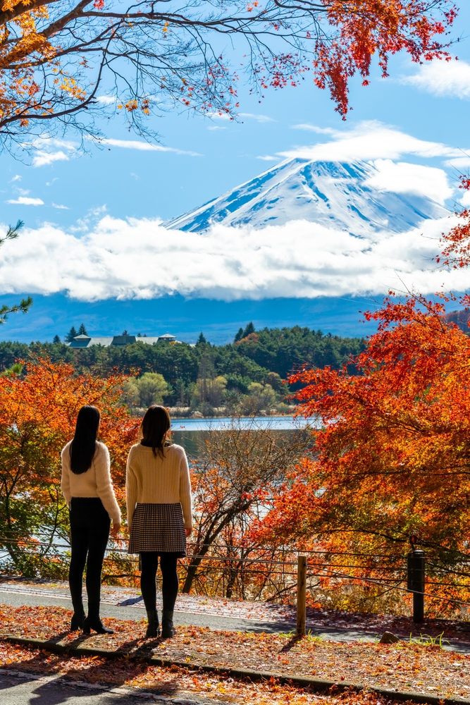 Two young women standing overlooking Mount Fuji on a sunny fall day.