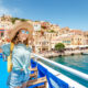 girl wearing sunhat sunglasses and a day pack in front of a mediterranean town mediterranean cruise packing list