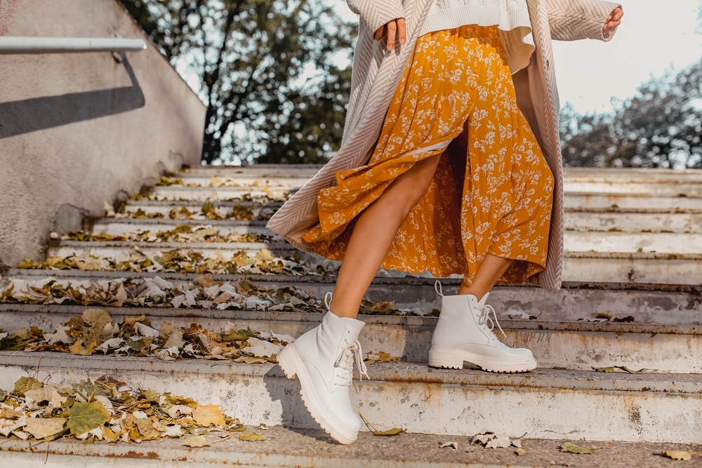 Waist down photo of a woman wearing a flowing orange dress and white sneakers on a set of stairs.