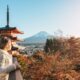 Woman in a coat showcasing what to wear in Japan in the fall stands looking out over fall foliage near a pagoda and Mount Fuji in the distance.