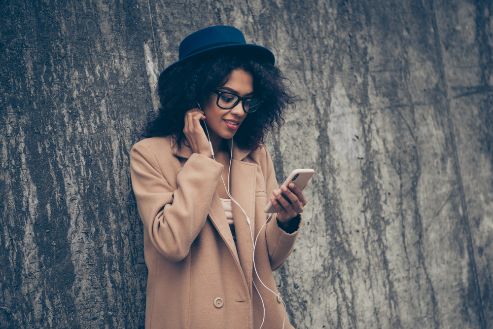 Charming curly-haired lady wearing cosy beige spring season cashmere topcoat outfit eyeglasses eyewear listening audio podcast 