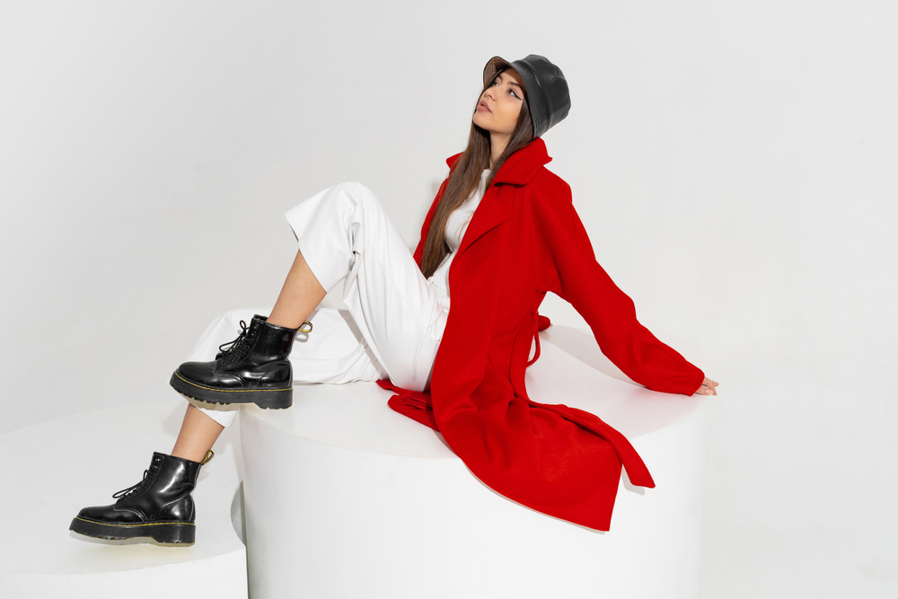 Fashionable model in stylish hat, red coat and boots posing on white background in studio. The article is about London in fall. 