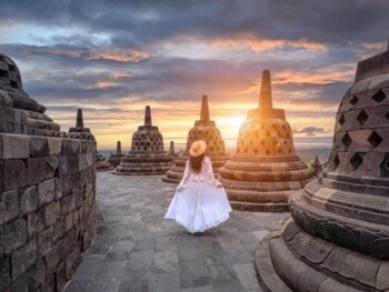 Girl in white maxi dress between the brown temple structures during the sunrise what to wear in bali