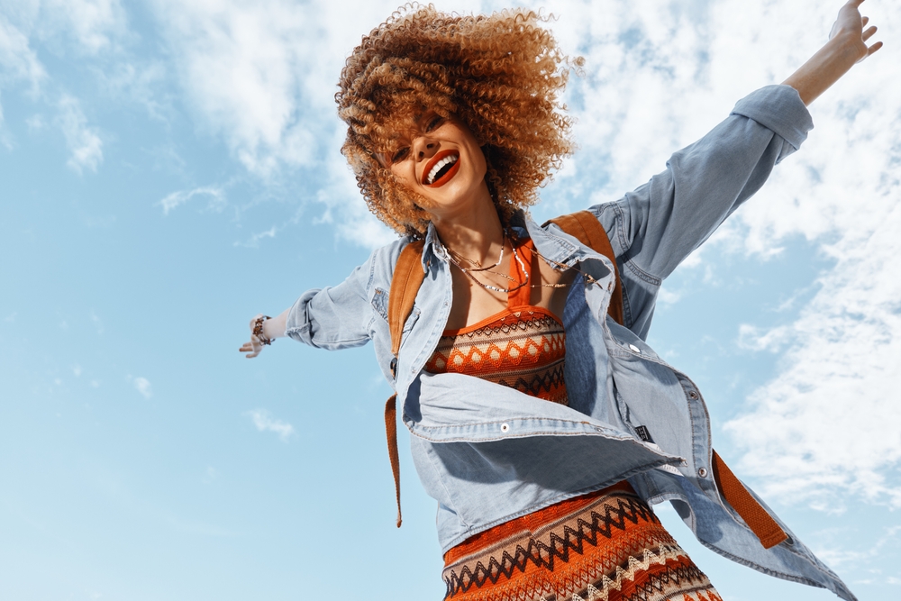 Joyful Traveler: Smiling Woman , Enjoying Happy Vacation with Backpack and Curly Hair under the Blue Sky