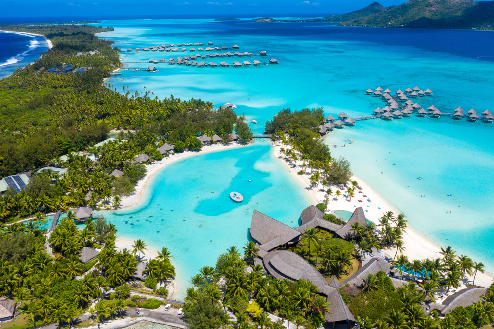 Aerial view of Bora Bora with crystal clear water, palm trees, and resorts.