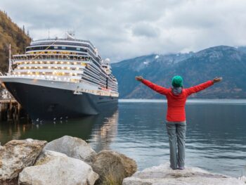 woman in red jacket green cap in front of a cruise ship alaska cruise outfits for july