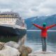woman in red jacket green cap in front of a cruise ship alaska cruise outfits for july