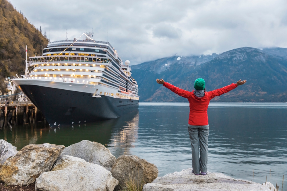 woman in red jacket green cap in front of a cruise ship alaska cruise outfits for july