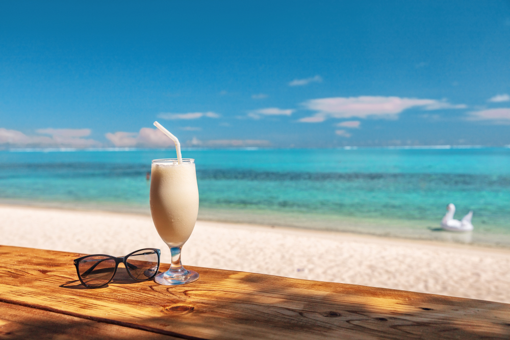 Pina colada and sunglasses sitting on a table with the bright blue ocean in the background.
